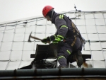 Skupina českolipských profesionálních hasičů přibíjí plechy na domě v Kamenickém Šenově